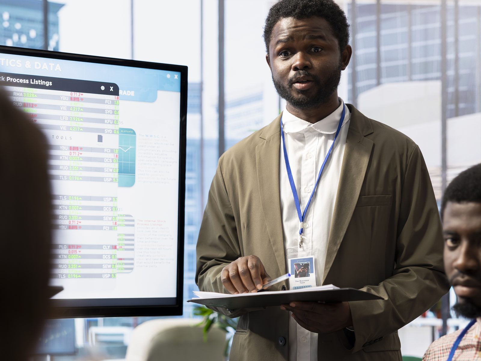 A presenter briefing colleagues in front of a screen showing analytics and data